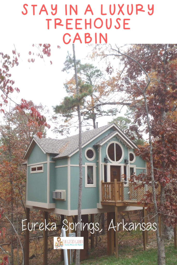 a blue treehouse cabin in Eureka Springs, Arkansas with trees around and a text overlay