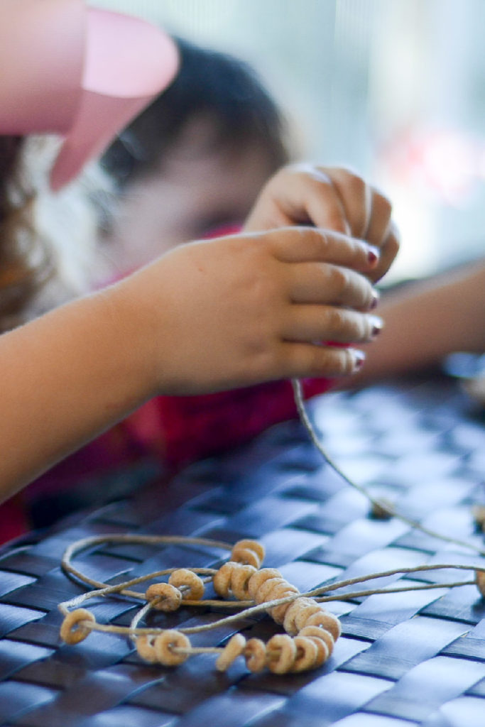little girl making a Cheerios garland for birds with string and Cheerios 