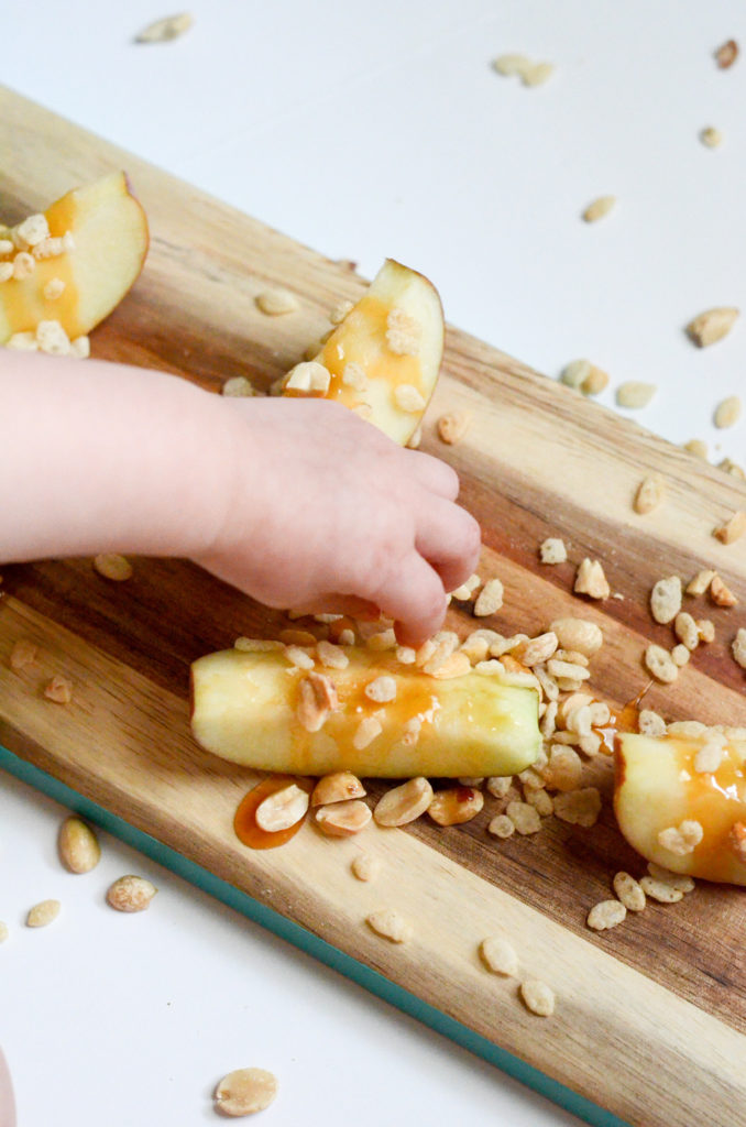 child sprinkles Rice Krispies cereal on apple slices with caramel 