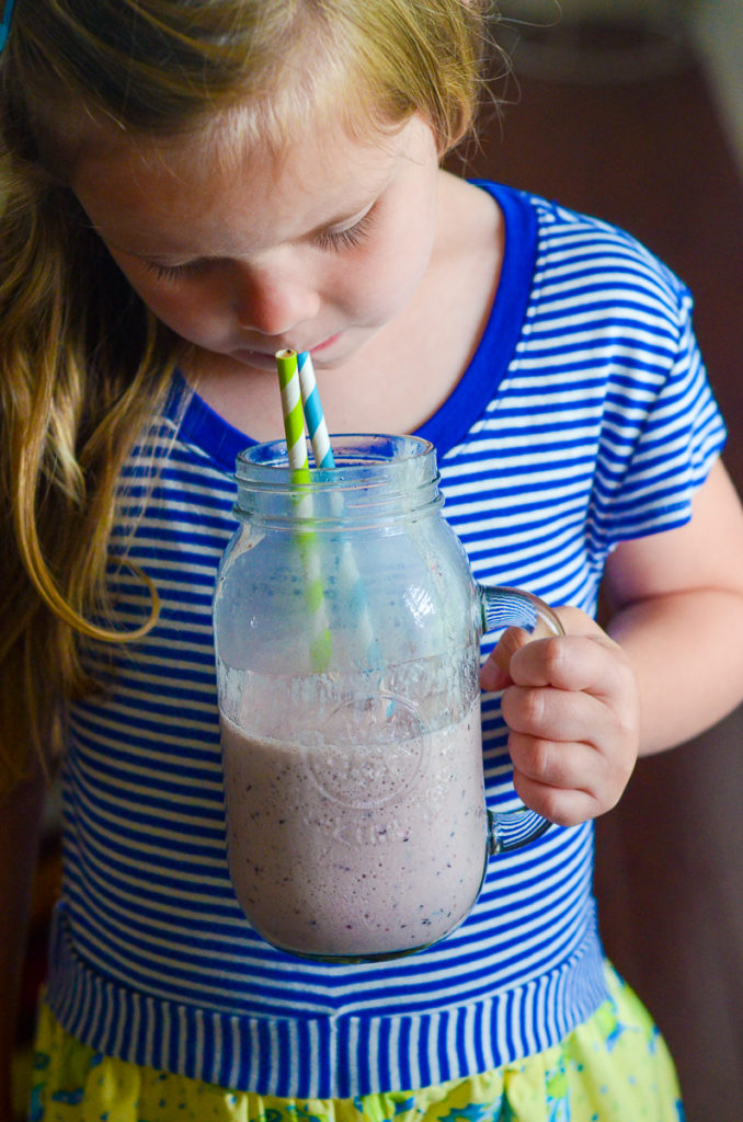 little girl drinks blue raspberry frozen lemonade from two straws