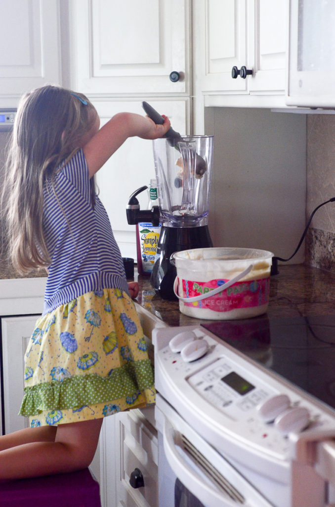 little girl scoops ice cream into a blender