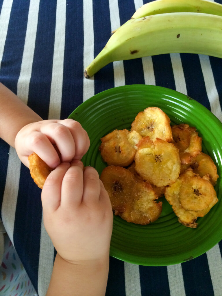 child's hands holding fried plantains (Panamanian patacones) over green plate