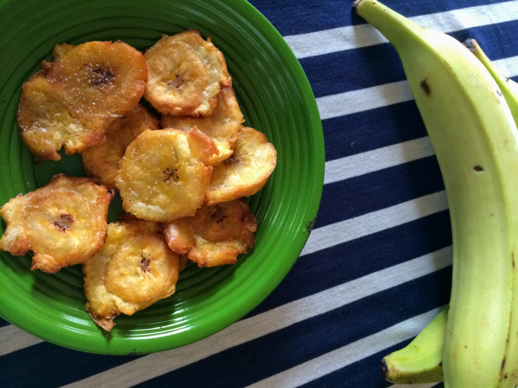 patacones de Panama - fried green plantains on green plate with plantains nearby