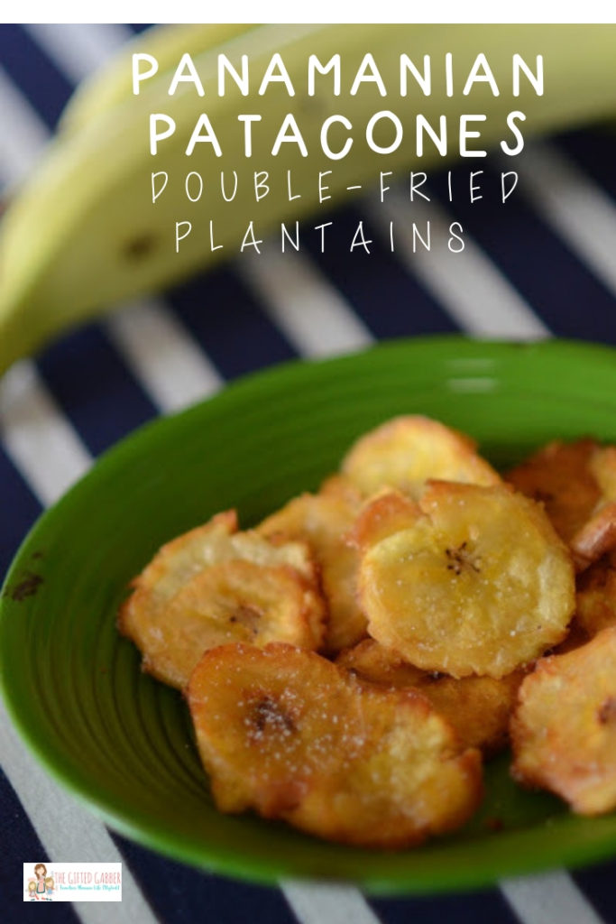 twice fried plantains - platanos verdes fritos - on a green plate with a striped tablecloth and green plantains in back
