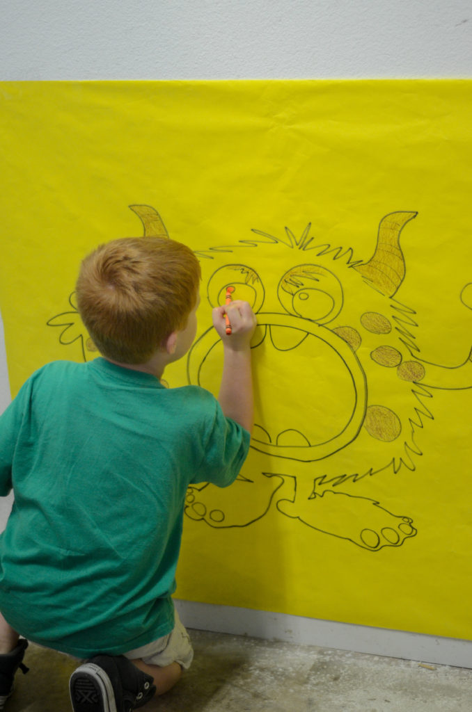 boy colors big monster drawing on wall at little monster birthday party