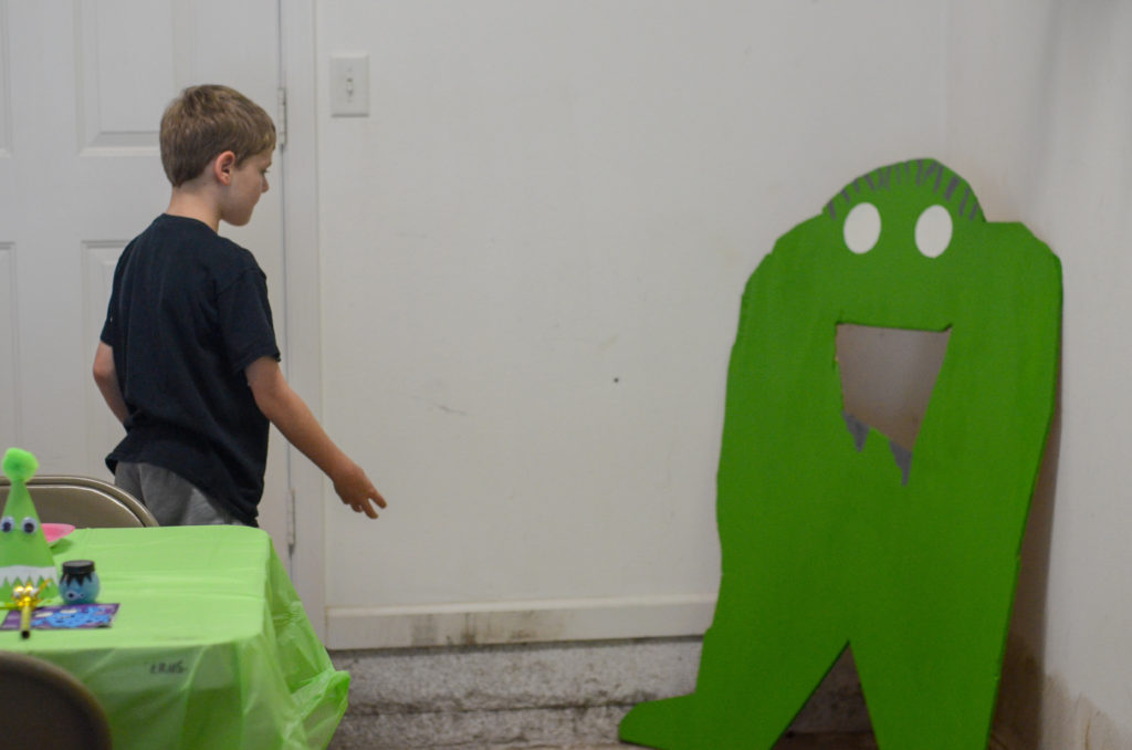 boy throws bean bag into wooden monster at monster themed party