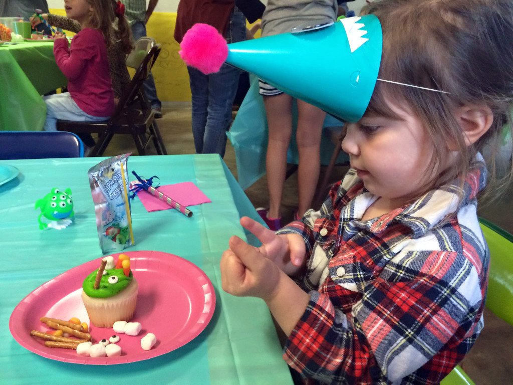 little girl wears monster party hat with a monster cupcake at a monster themed birthday party