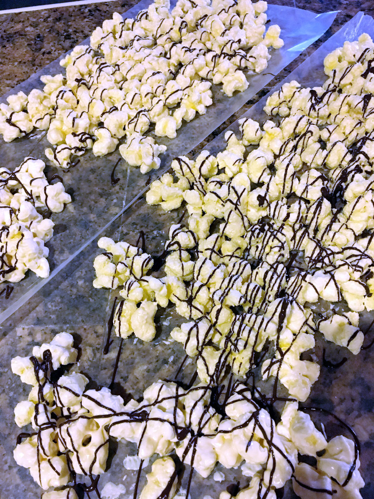 batches of white chocolate popcorn on counter with a chocolate drizzle 