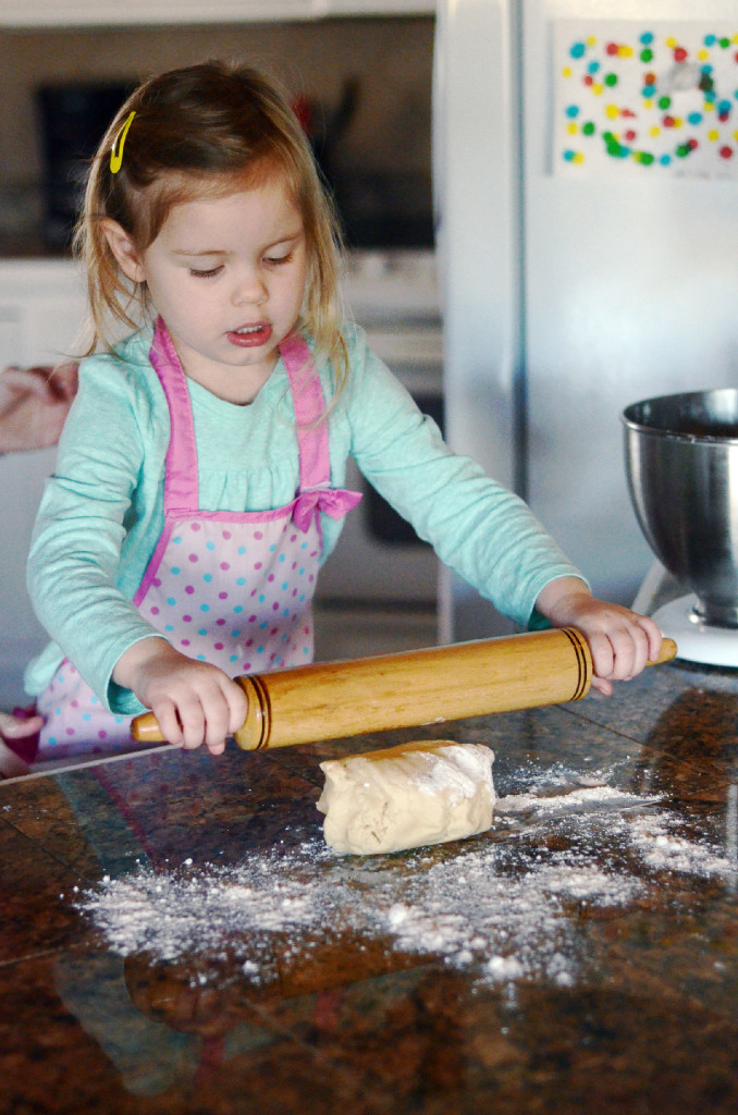 little girl rolling cookie dough with rolling pin in kitchen 