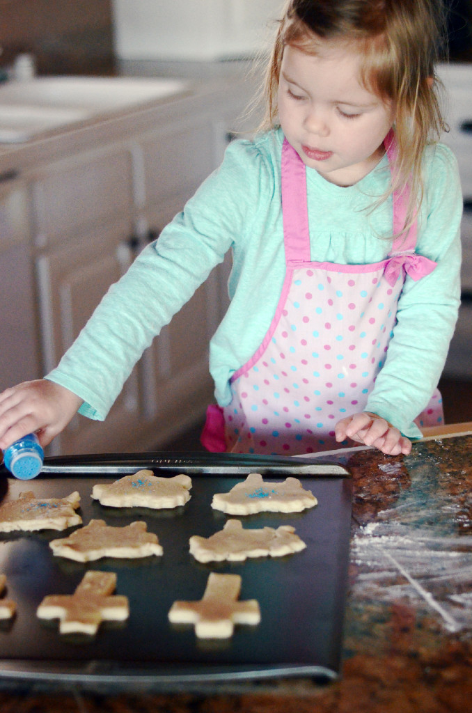 little girl adding sprinkles to Easter lamb cookies
