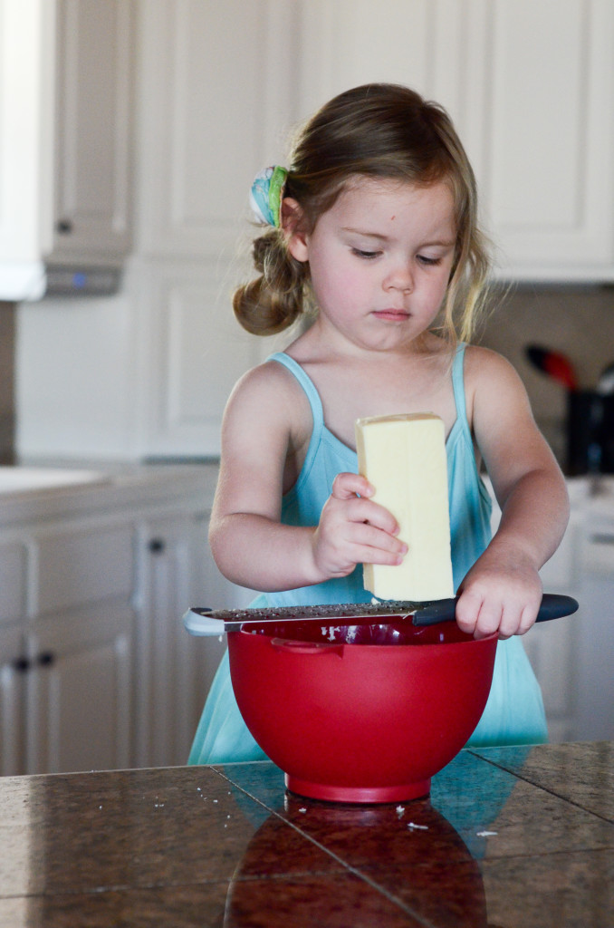 little girl helps make migas con huevos by grating cheese