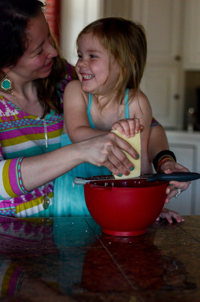 mother and daughter grate cheese over red bowl in kitchen 