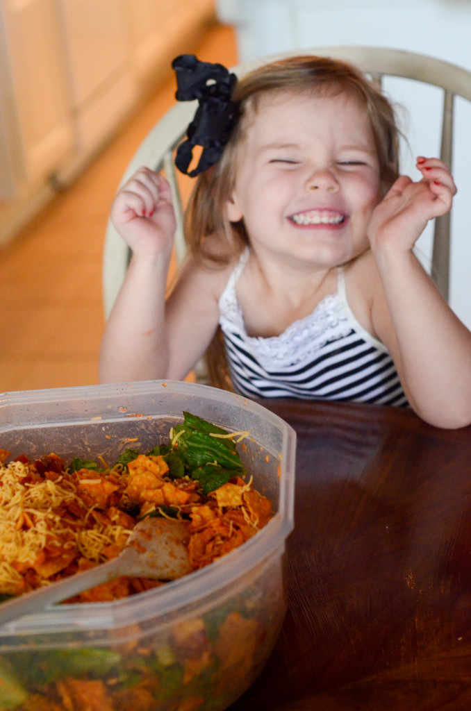 little girl smiles at table beside big salad bowl 