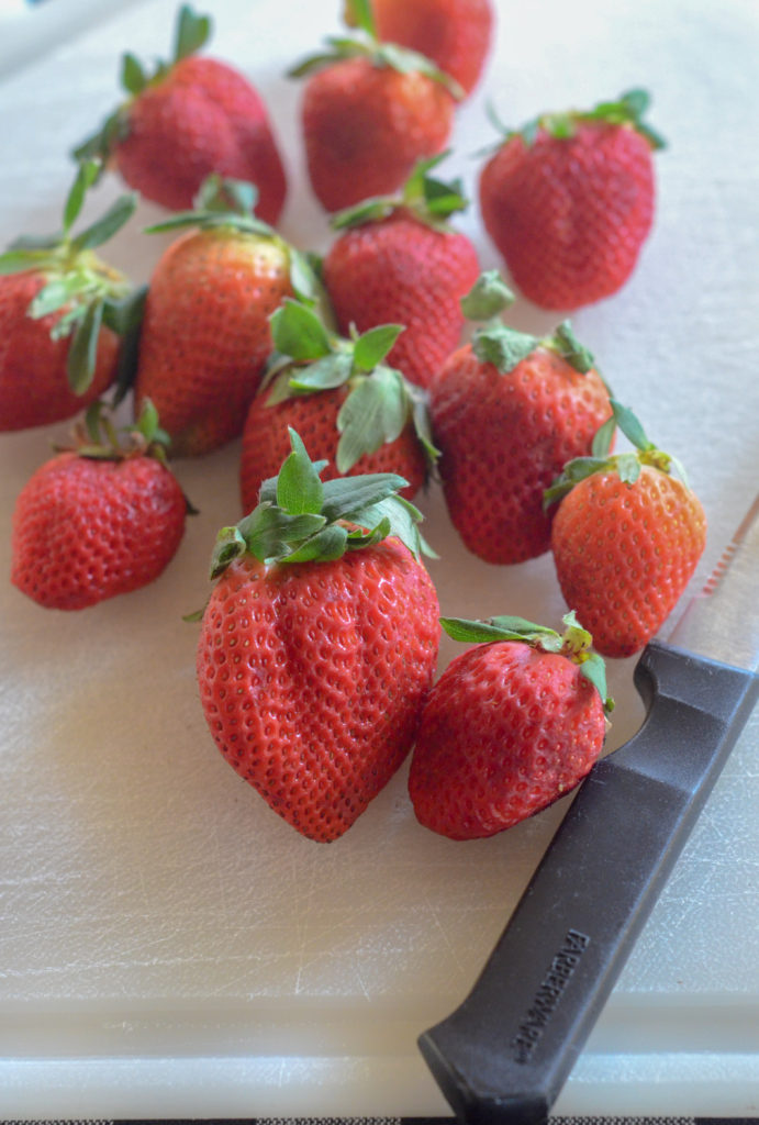 strawberries and knife on plastic cutting board