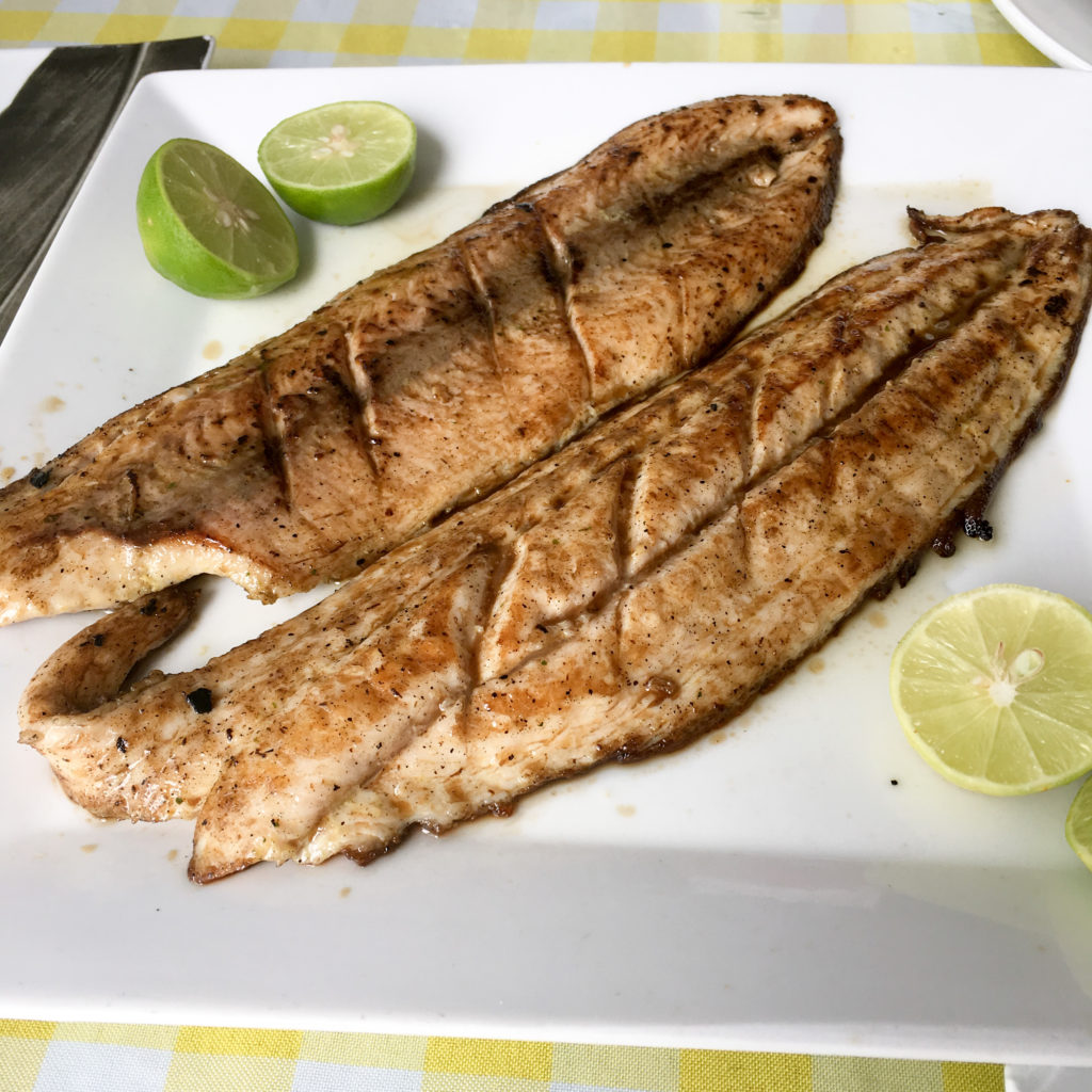 grilled fish on a white plate with limes 