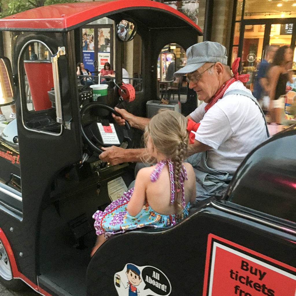 little girl riding with train conductor on Branson Landing train 
