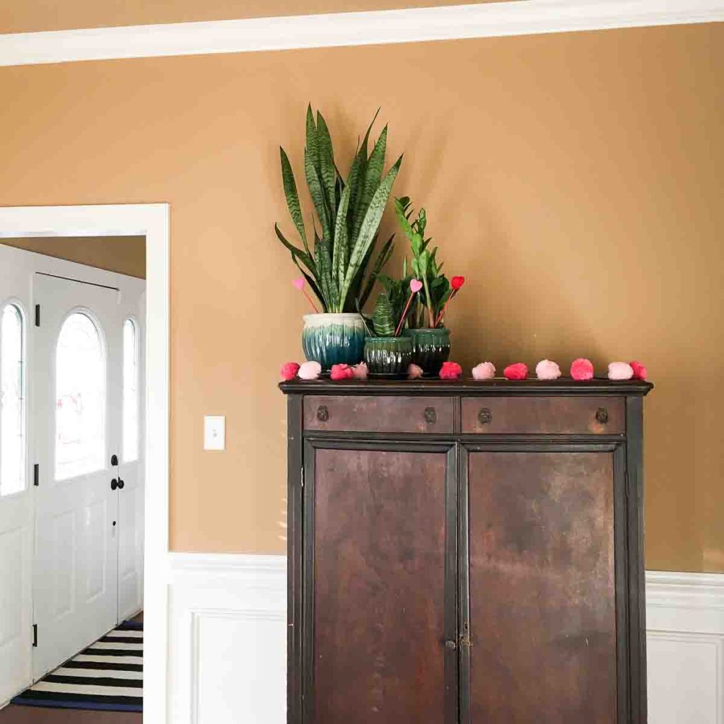 plants on top of an armoire with a pom pom garland in a Valentine's home tour