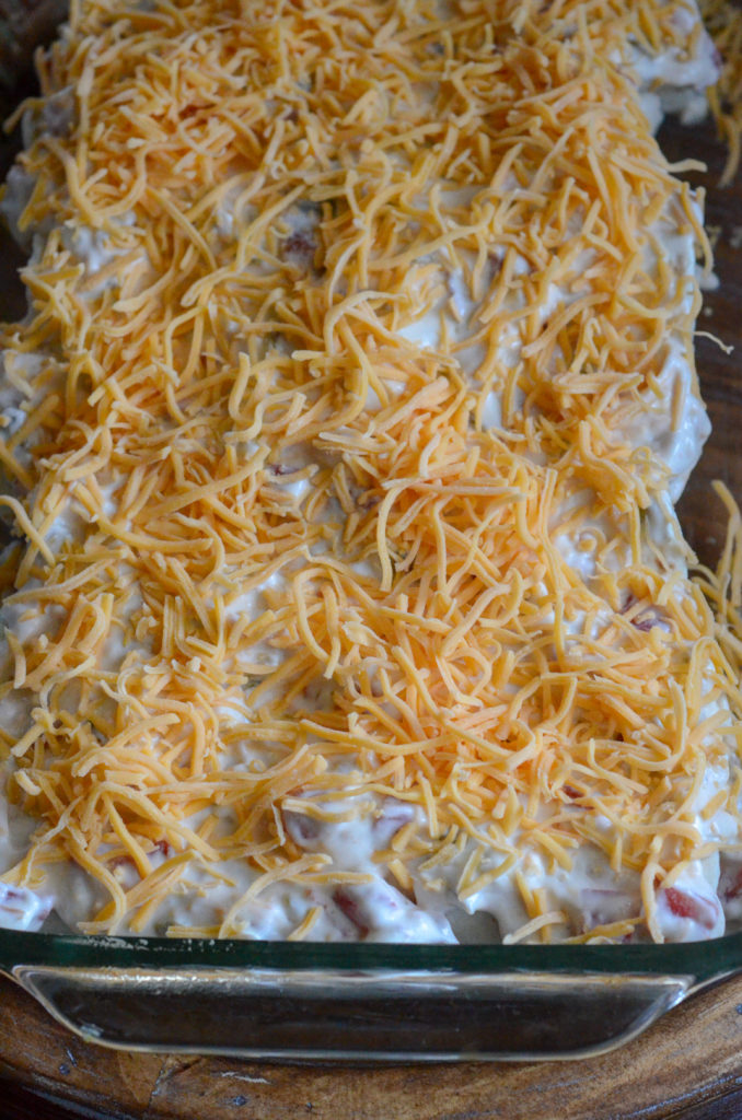 pan of unbaked sour cream chicken enchiladas with shredded cheddar on top