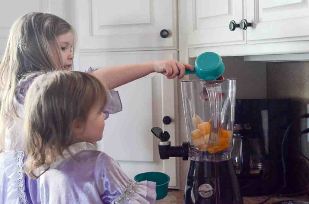 little girls make strawberry banana smoothie with orange juice in blender