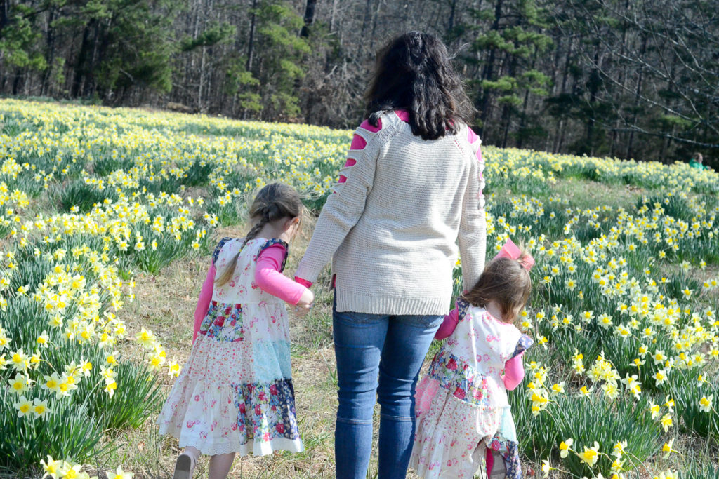 a mother and her two young daughters walk in a field of flowers 