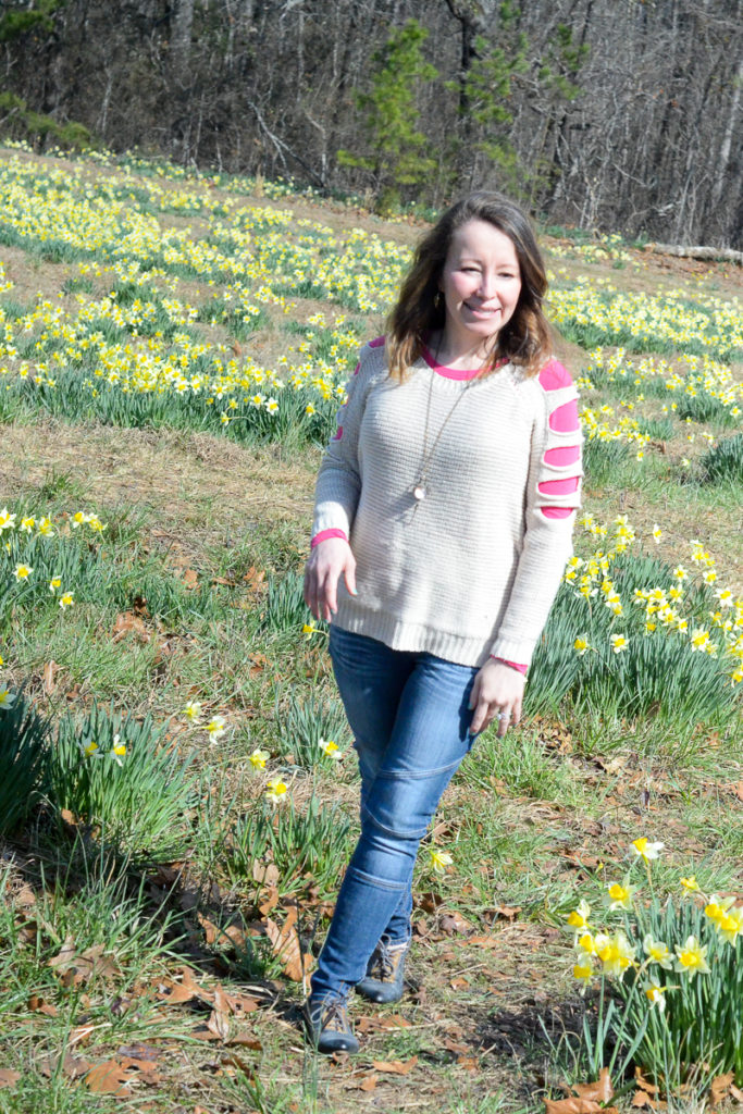 woman in sweater and jeans poses in a field of daffodils 