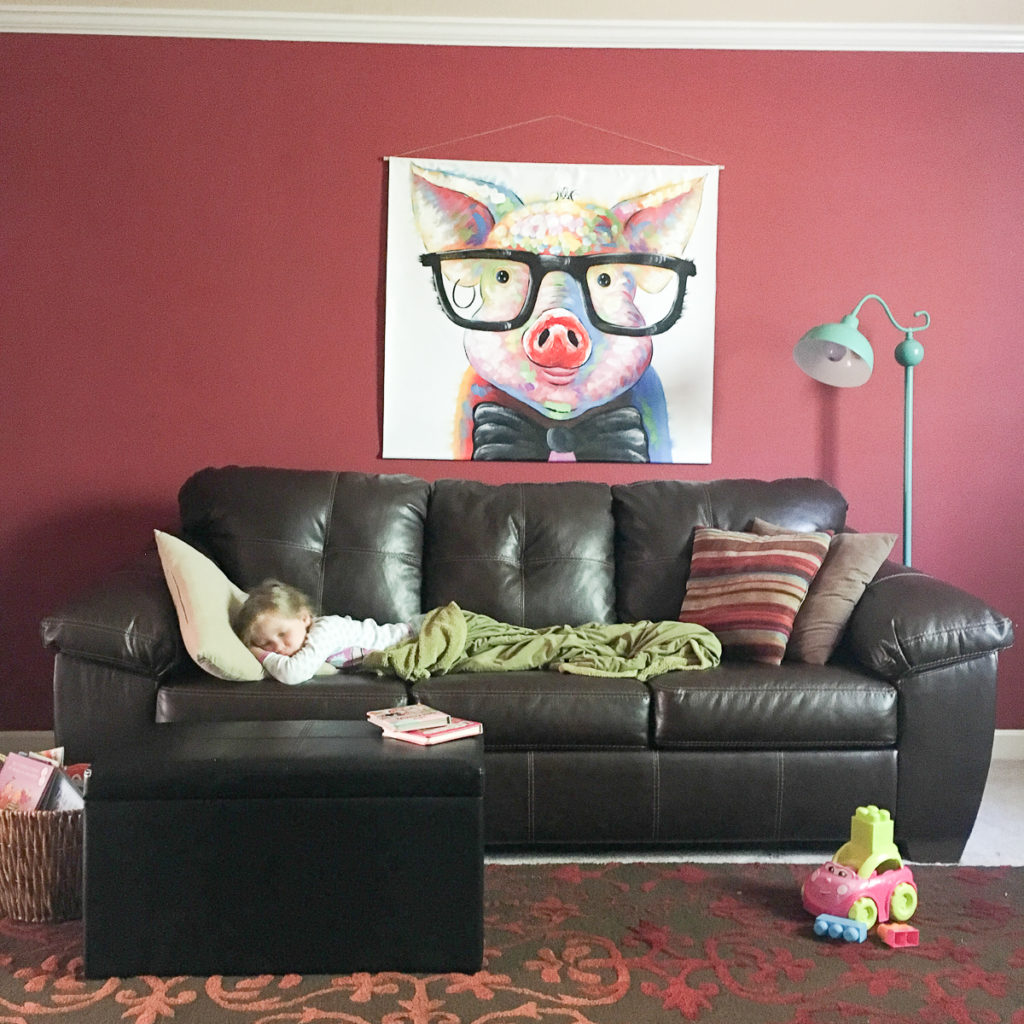 an unframed canvas scroll art with large pig art hangs above brown sofa against red wall 