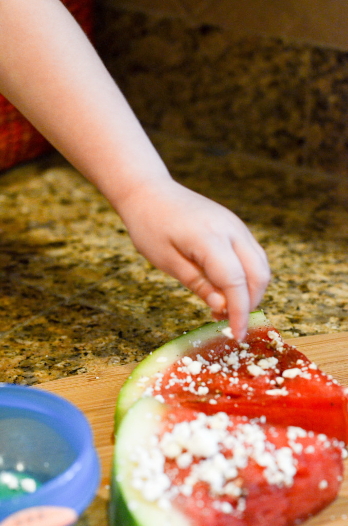 child adds feta cheese to a fruit pizza 