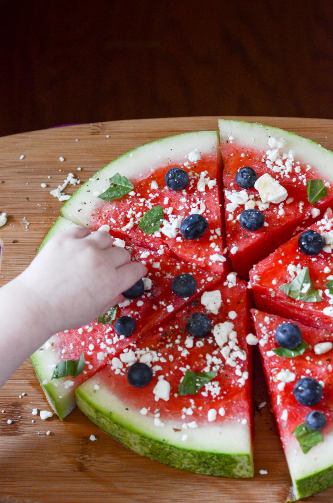 child's hand drops blueberries on watermelon pizza 
