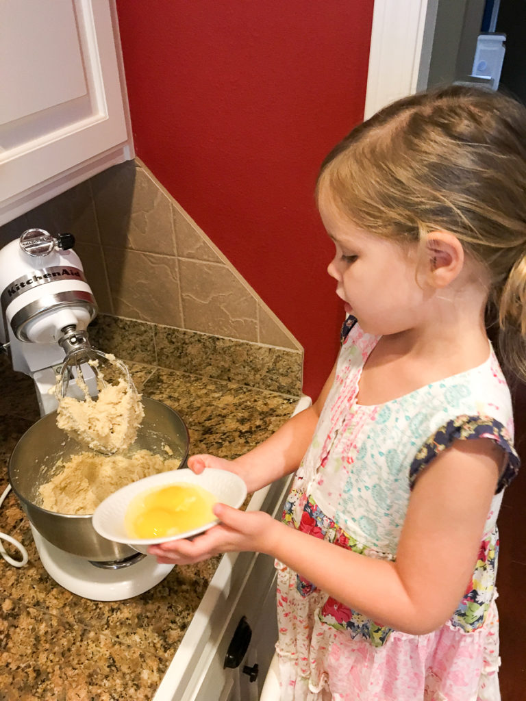 young girl pours egg into stand mixer 