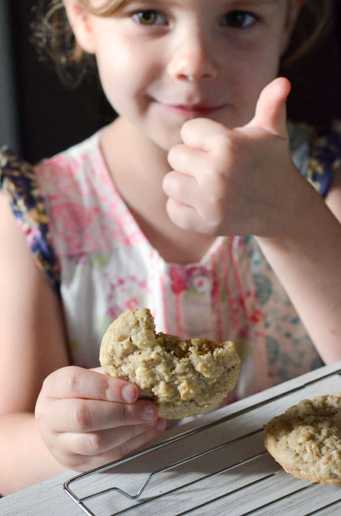 little girl eats cookie and gives thumbs up sign 