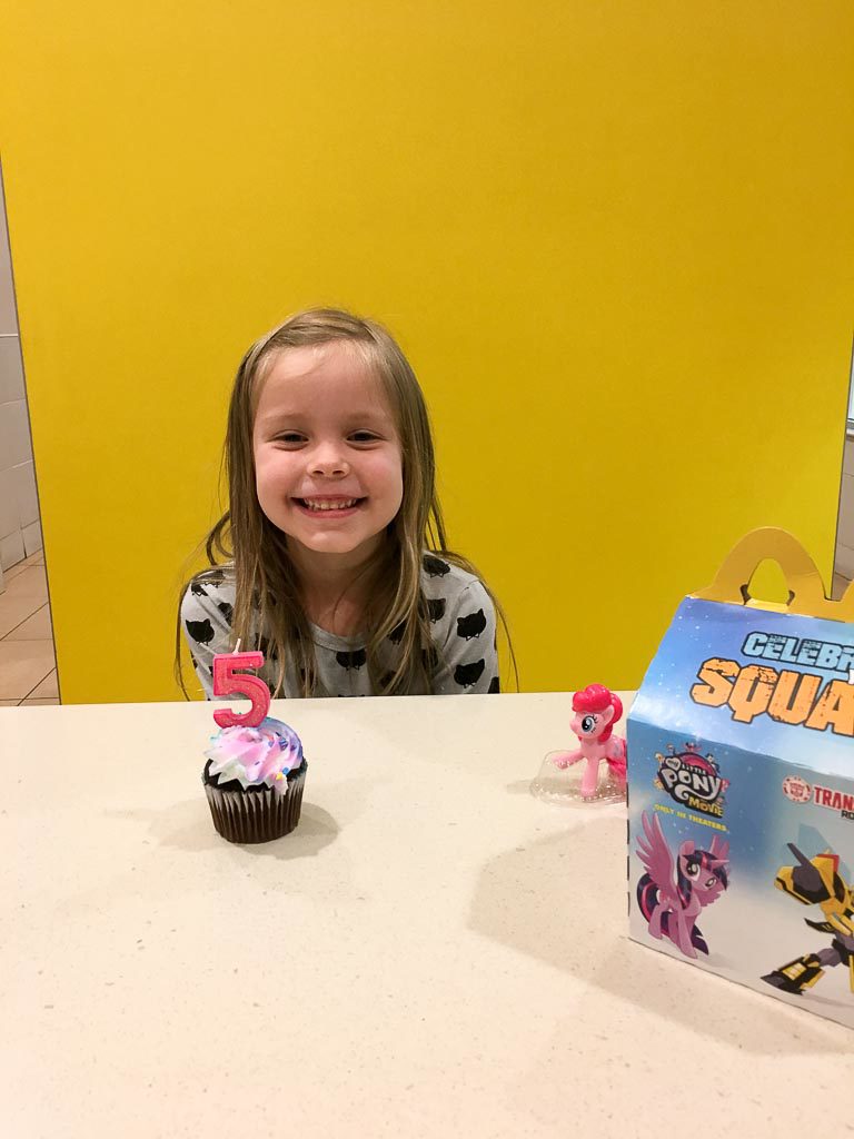 little girl smiles with a cupcake and a Happy Meal at her McDonald's birthday party 