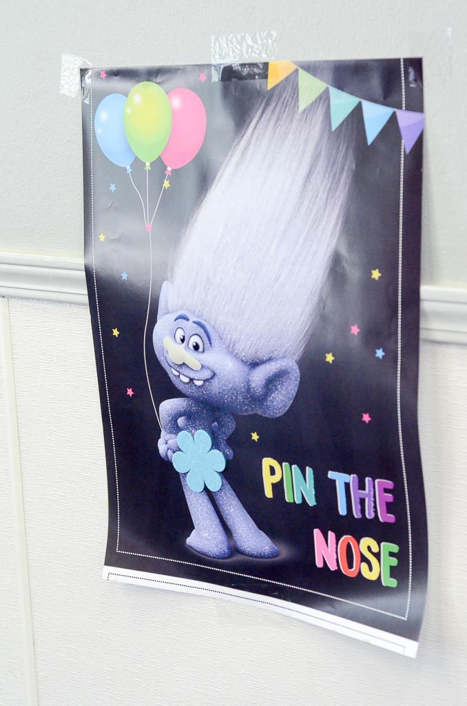 Trolls party games for kids - Pin the Nose on Branch hangs on the wall of a Trolls birthday party 
