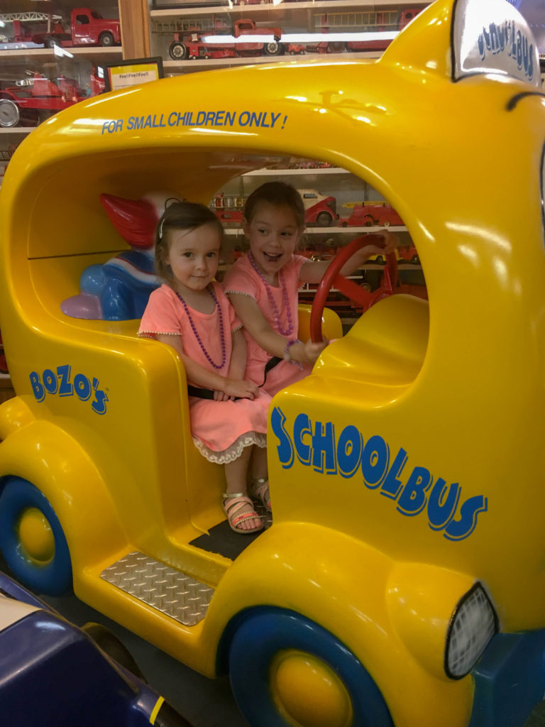 two sisters ride in Bozo's School Bus car at the Toy Museum in Branson