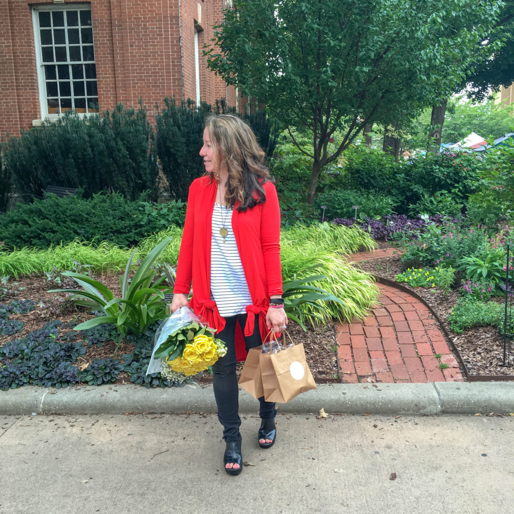 teacher wears bright red cardigan with striped tank and holds bouquet of flowers in town square 