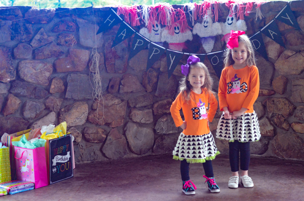 two girls stand in front of cute ghost decorations for a girl's Halloween party