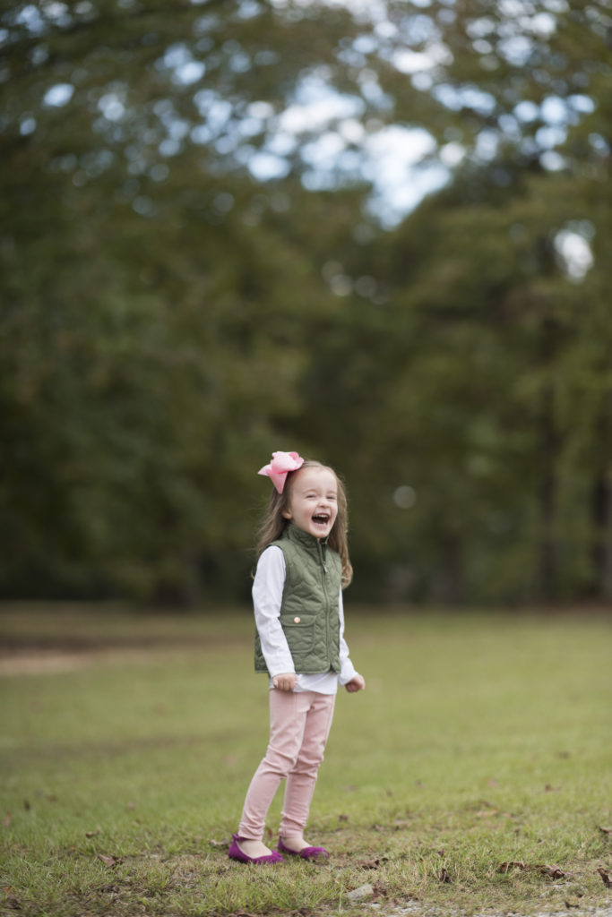 little girl in pink pants and green vest smiling for camera 