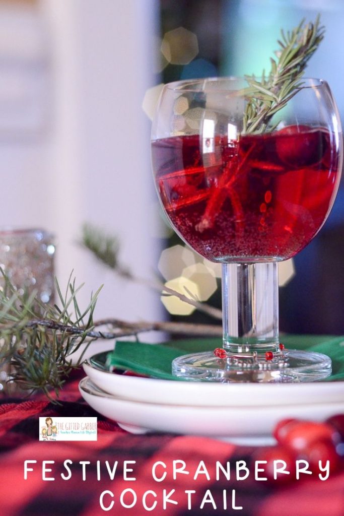 glass of cranberry cocktail atop two cocktail plates with Christmas decor in back
