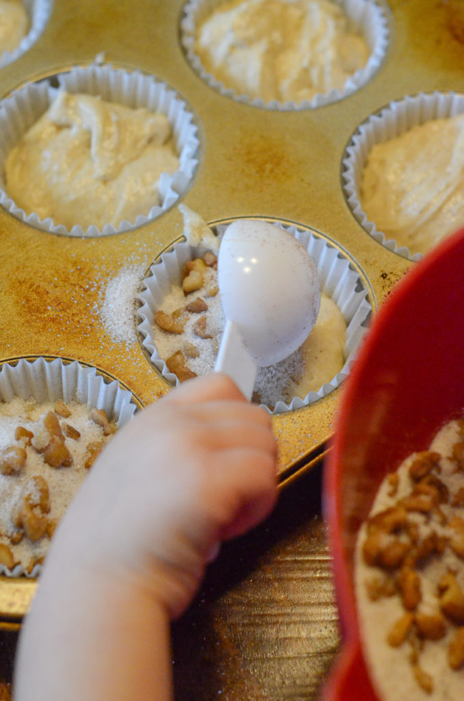 small child's hand pouring cinnamon sugar on buttermilk spice muffins 