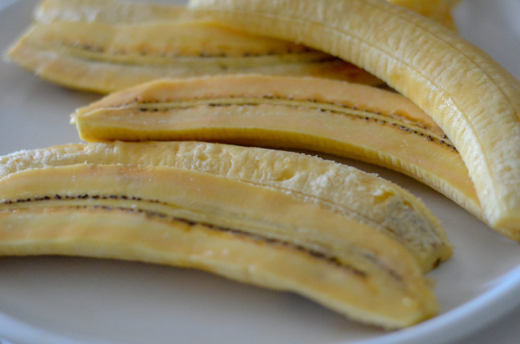 ripe plantains peeled and sliced lengthwise on white plate 
