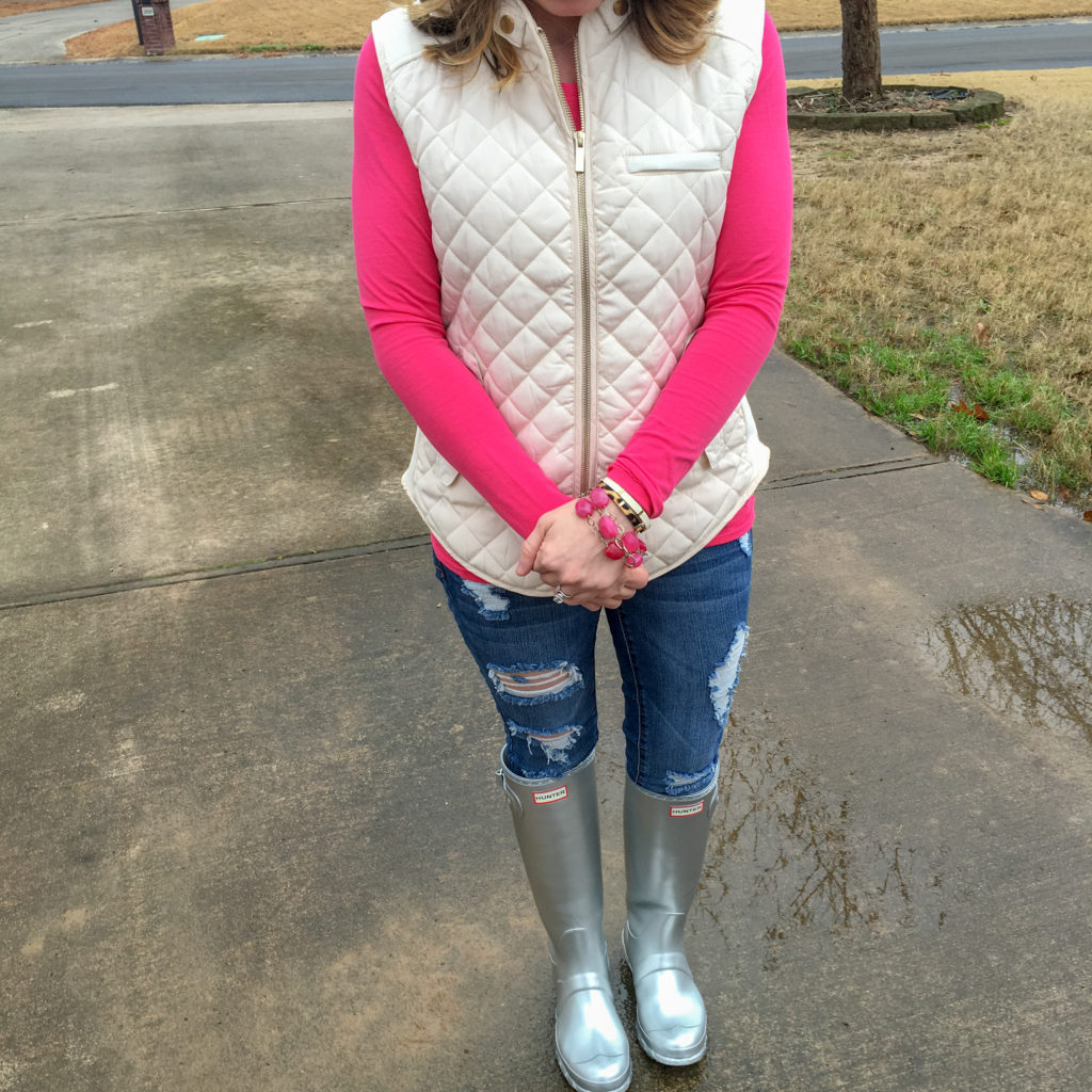 woman stands in silver Hunter rainboots, white quilted vest, shredded jeans, and pink top to show ideas for layering clothes for puffer vest outfit