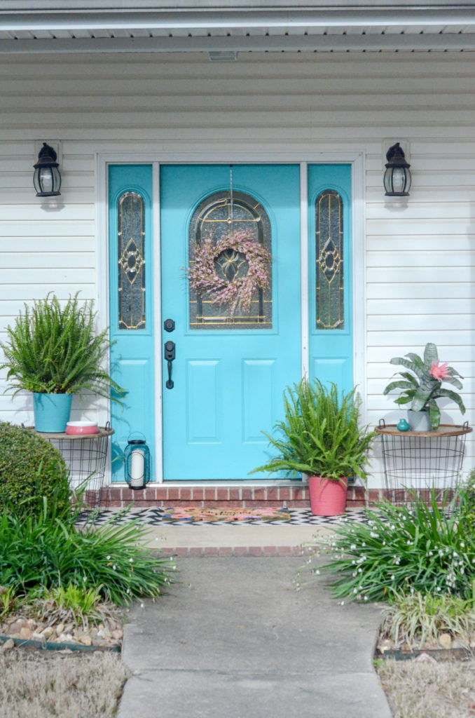 pink porch decor and teal porch decor adorning a painted front porch door, including Queen Anne ferns on front porch and a blooming pink bromeliad plant