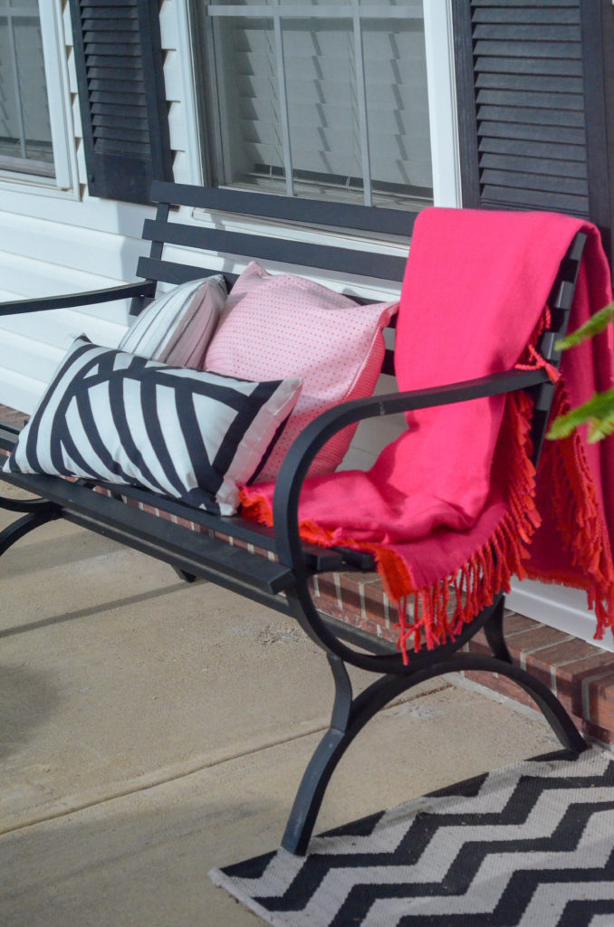 front porch benches draped with pink tassled blankets and pink and black and white pillows