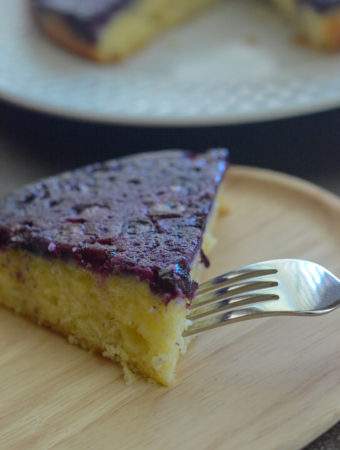 piece of blueberry upside down cake on wooden plate with fork