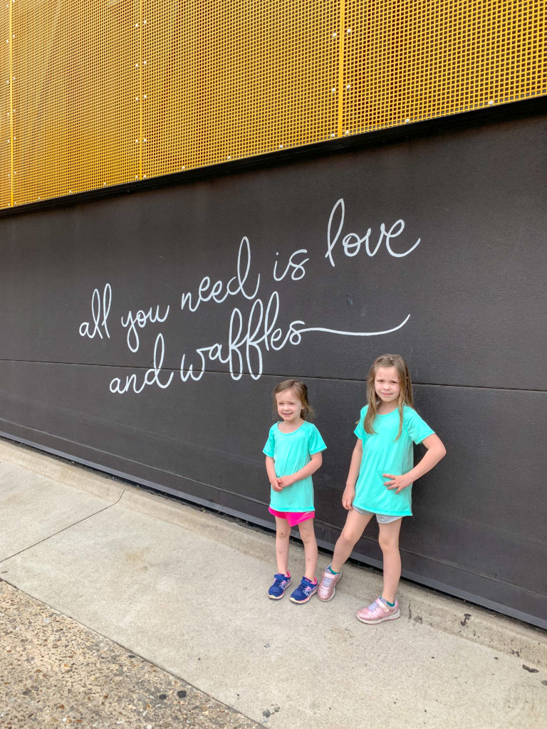two girls stand in front of Waffle Champion wall - Oklahoma City with Kids