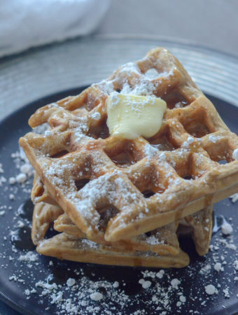 cinnamon waffles on black plate with butter and powdered sugar