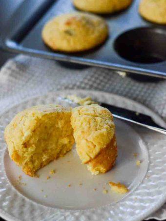 cornbread muffin standing on plate with knife and muffin tin in background