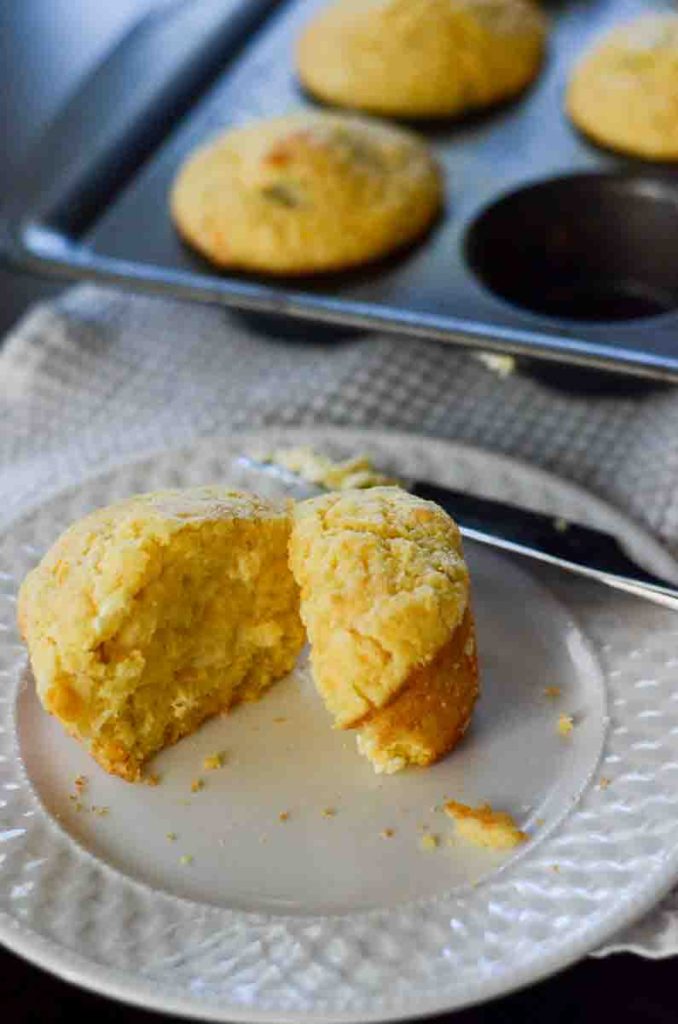 cornbread muffin standing on plate with knife and muffin tin in background 