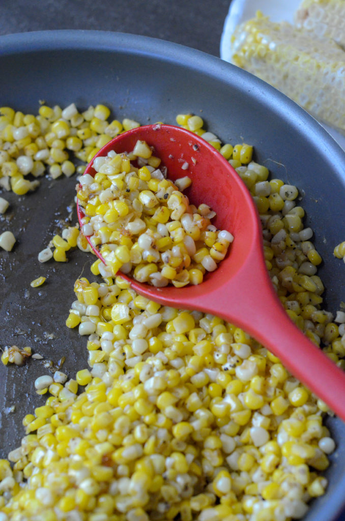 fried skillet corn on a red spoon in a pan 