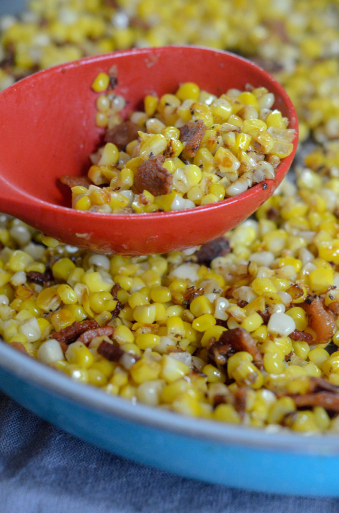 fried southern corn with bacon in a blue skillet with a red spoon