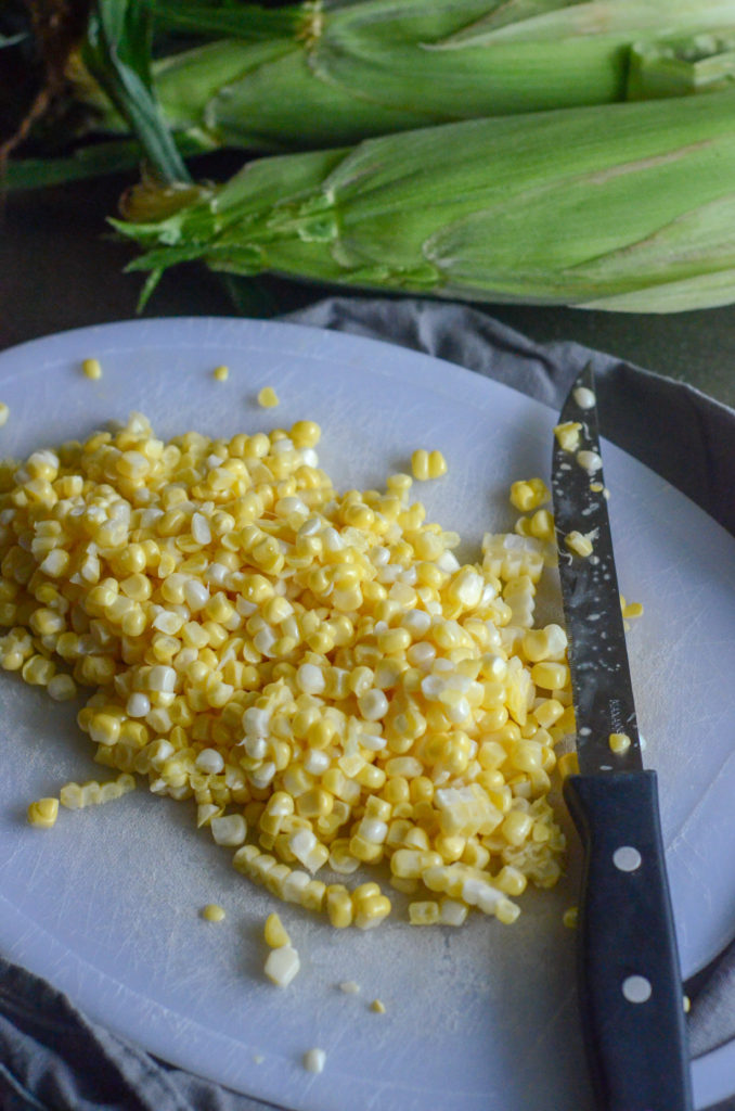 shucked corn on a cutting board with a knife